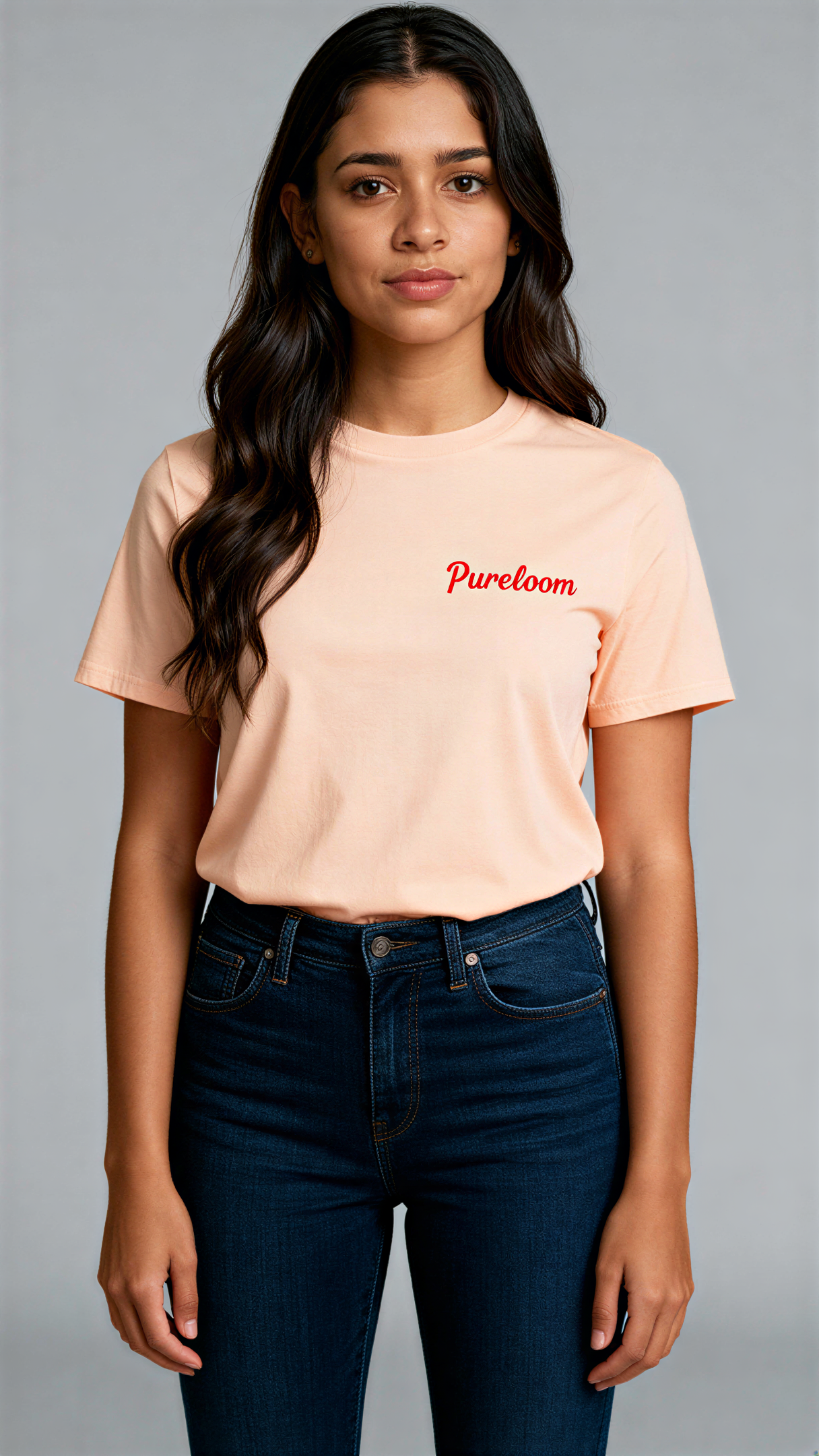 במבט קדמי, אישה לובשת חולצת כותנה אורגנית בצבע ורוד עם לוגו אדום "Pureloom" בצד שמאל של החזה מבית פיורלום.