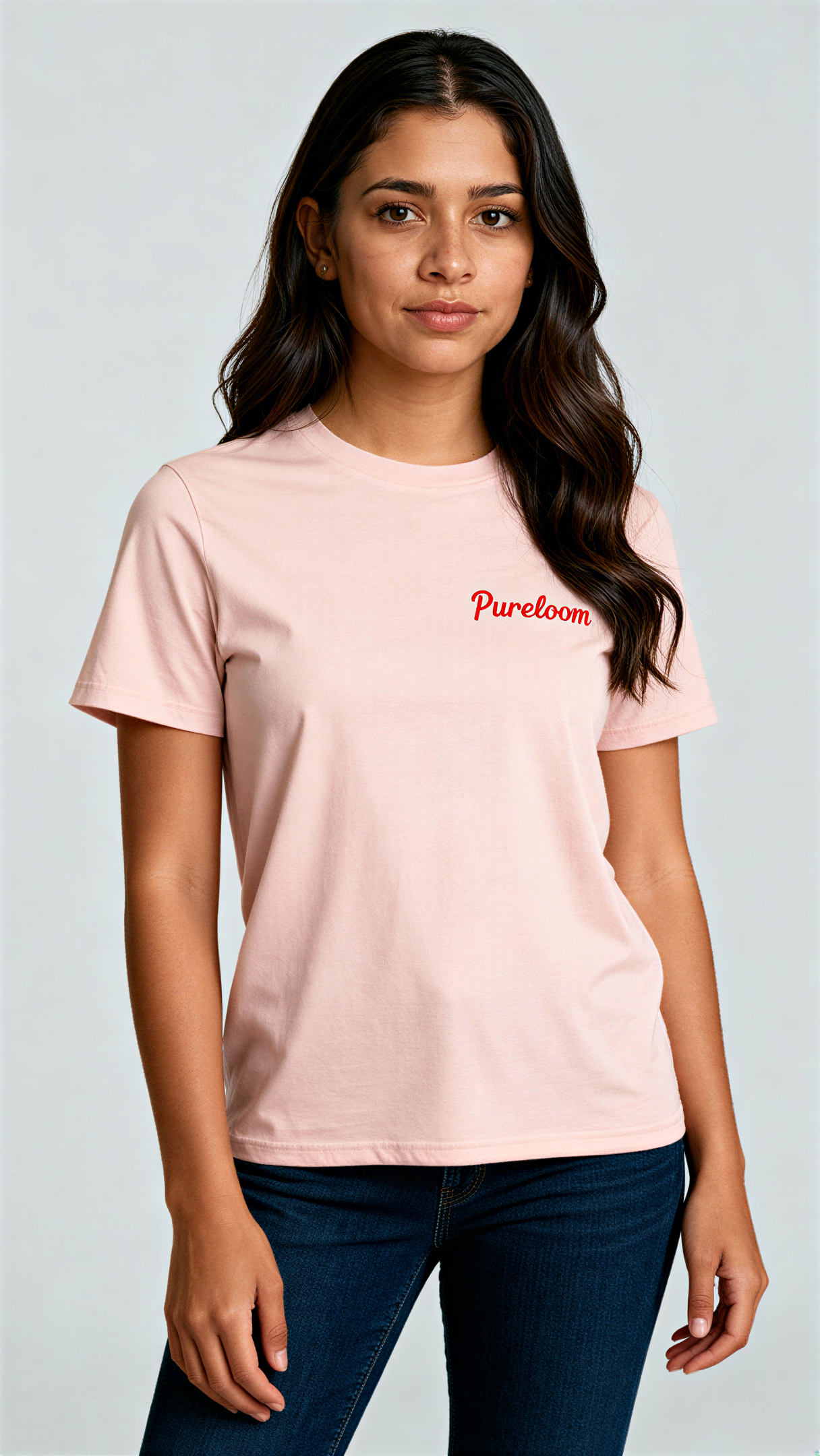 במבט קדמי, אישה לובשת חולצת כותנה אורגנית בצבע ורוד עם לוגו אדום "Pureloom" בצד שמאל של החזה מבית פיורלום.