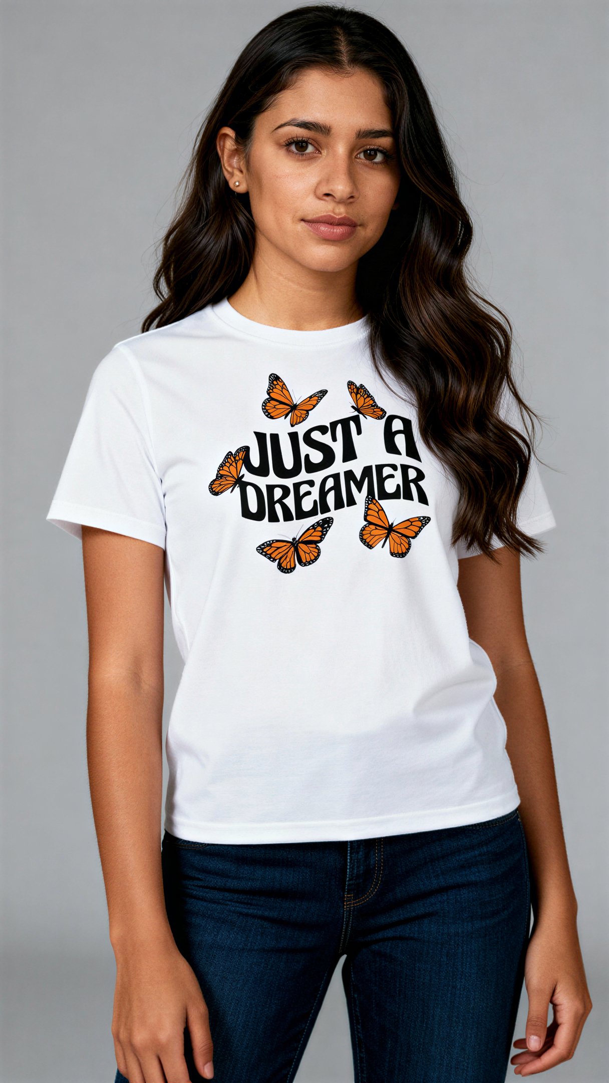 במבט קדמי, אישה לובשת חולצת כותנה אורגנית לבנה עם הדפס של פרפרים כתומים וכיתוב שחור גדול "Just a Dreamer" מבית פיורלום.