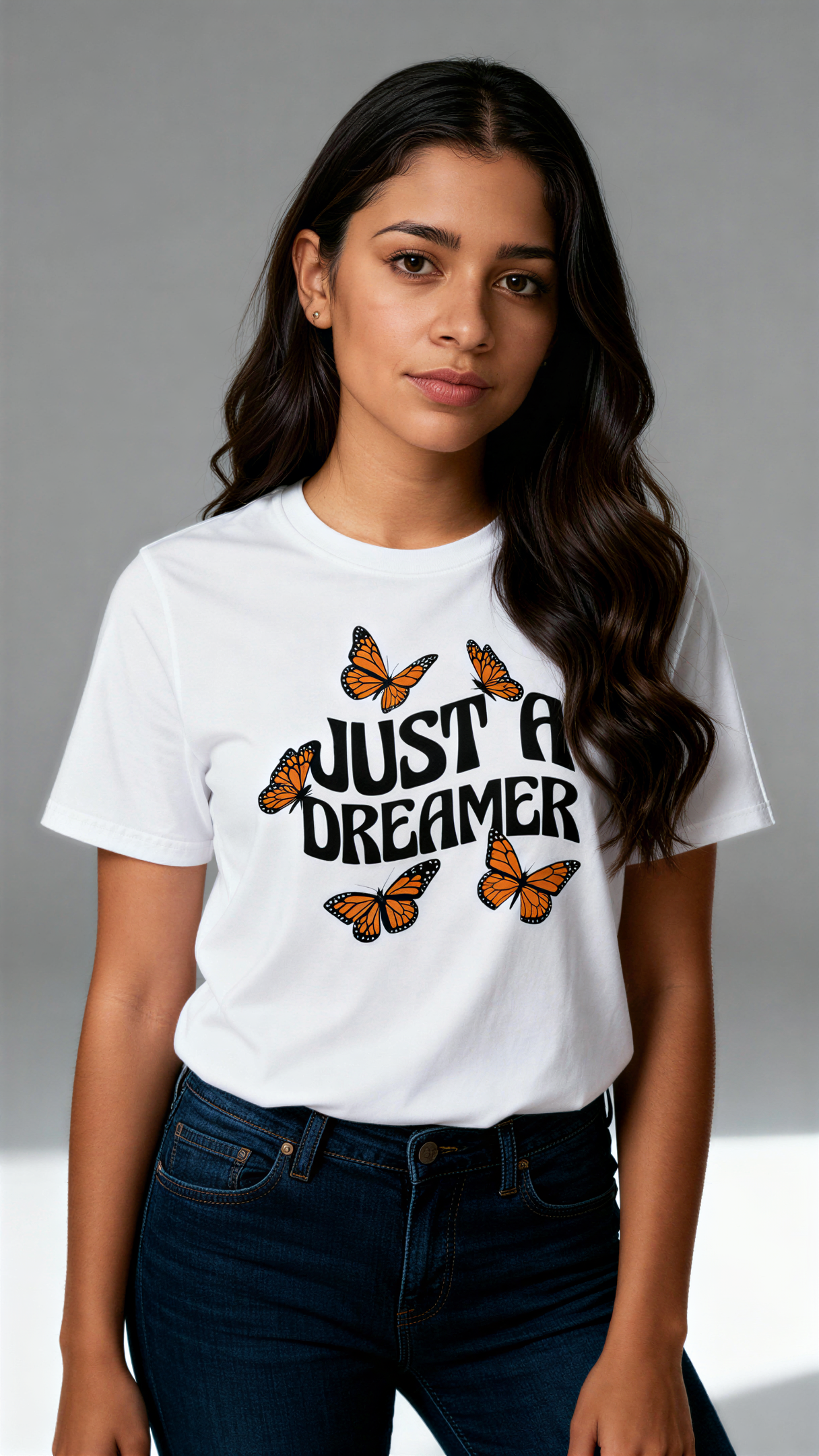 במבט קדמי, אישה לובשת חולצת כותנה אורגנית לבנה עם הדפס של פרפרים כתומים וכיתוב שחור גדול "Just a Dreamer" מבית פיורלום.
