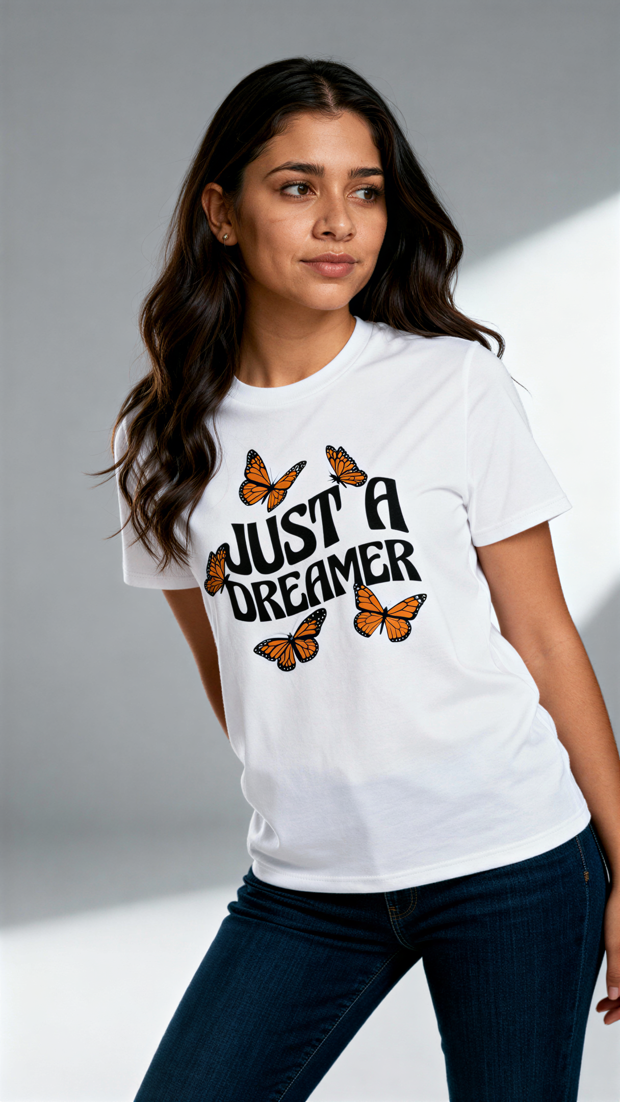 במבט קדמי, אישה לובשת חולצת כותנה אורגנית לבנה עם הדפס של פרפרים כתומים וכיתוב שחור גדול "Just a Dreamer" מבית פיורלום.