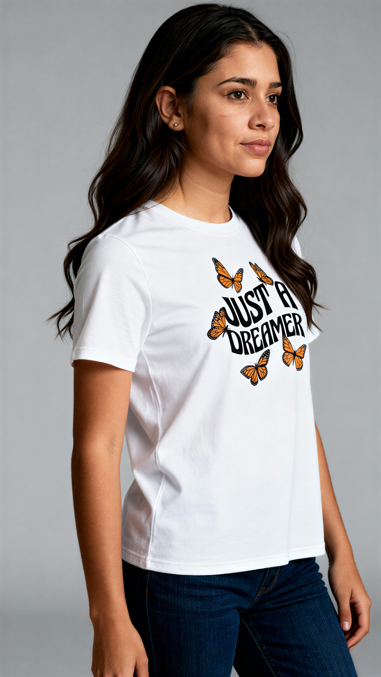 במבט צדדי, אישה לובשת חולצת כותנה אורגנית לבנה עם הדפס של פרפרים כתומים וכיתוב שחור גדול "Just a Dreamer" מבית פיורלום.