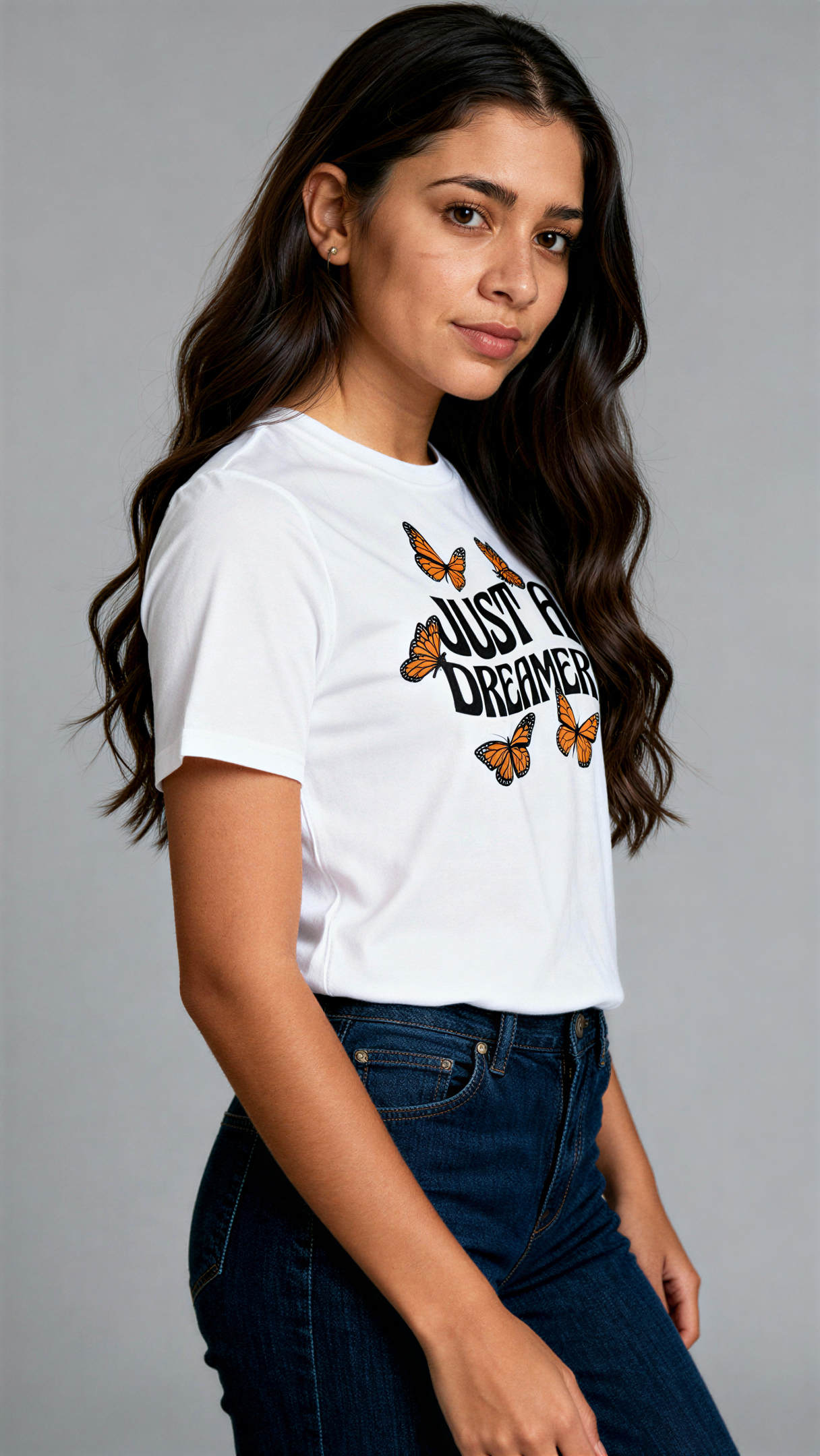 במבט צדדי, אישה לובשת חולצת כותנה אורגנית לבנה עם הדפס של פרפרים כתומים וכיתוב שחור גדול "Just a Dreamer" מבית פיורלום.