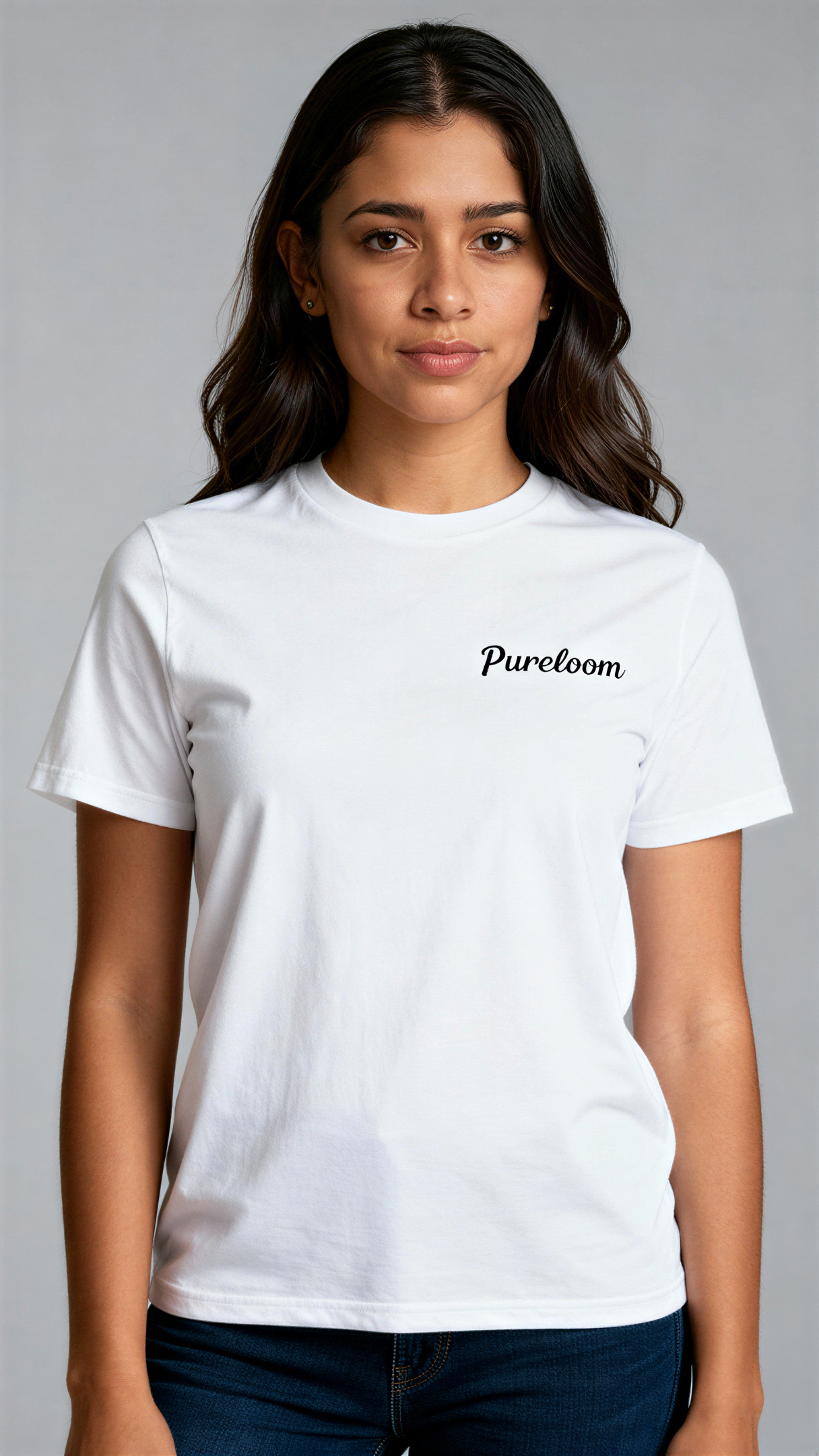 במבט קדמי, אישה לובשת חולצת כותנה אורגנית לבנה עם לוגו שחור "Pureloom" בצד שמאל של החזה מבית פיורלום.