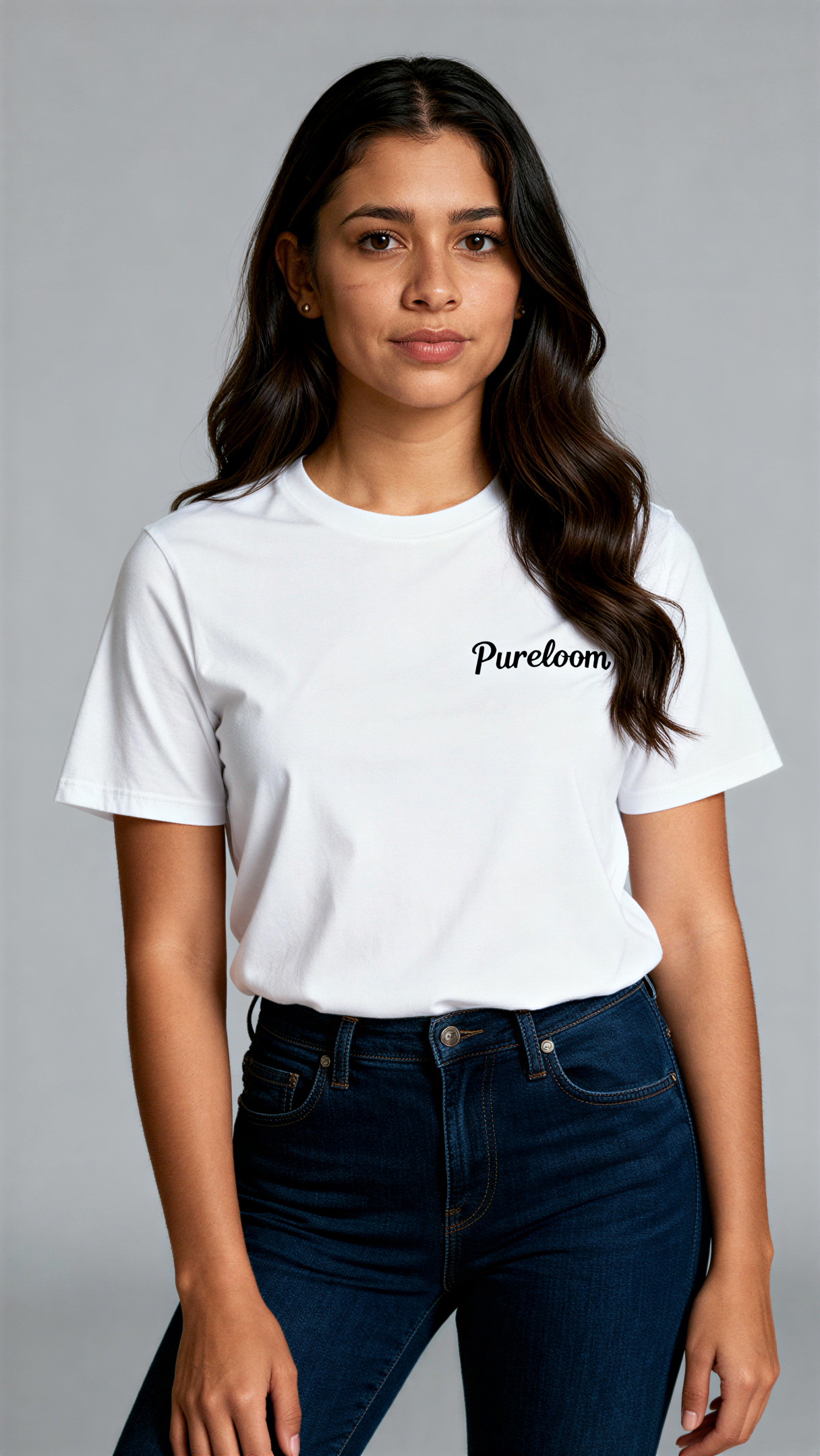 במבט קדמי, אישה לובשת חולצת כותנה אורגנית לבנה עם לוגו שחור "Pureloom" בצד שמאל של החזה מבית פיורלום.